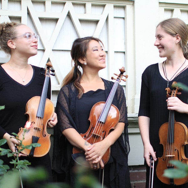 3 students smiling and holding their instruments near flowers