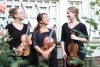 3 students smiling and holding their instruments near flowers